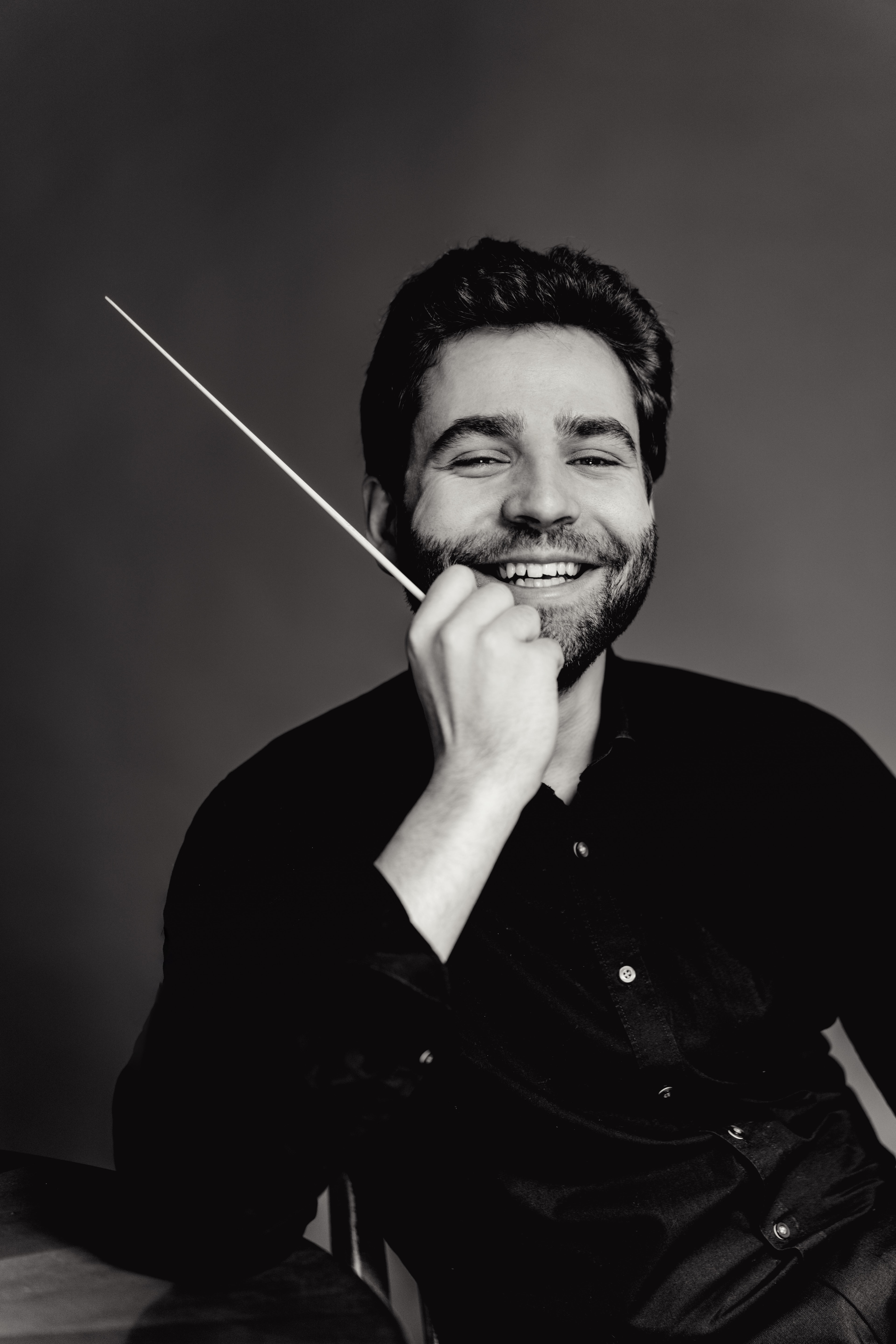 Simon Edelmann smiling, black and white portrait with baton (photo: Andrej Grilc)